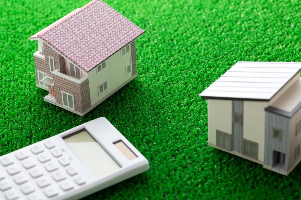 人工芝の上に置かれた2軒の住宅模型と電卓