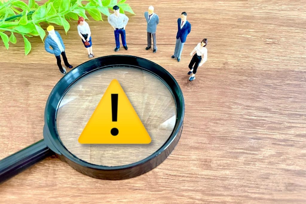 注意を示すプレートの上に置かれた虫眼鏡と周りを囲む人々のミニチュア