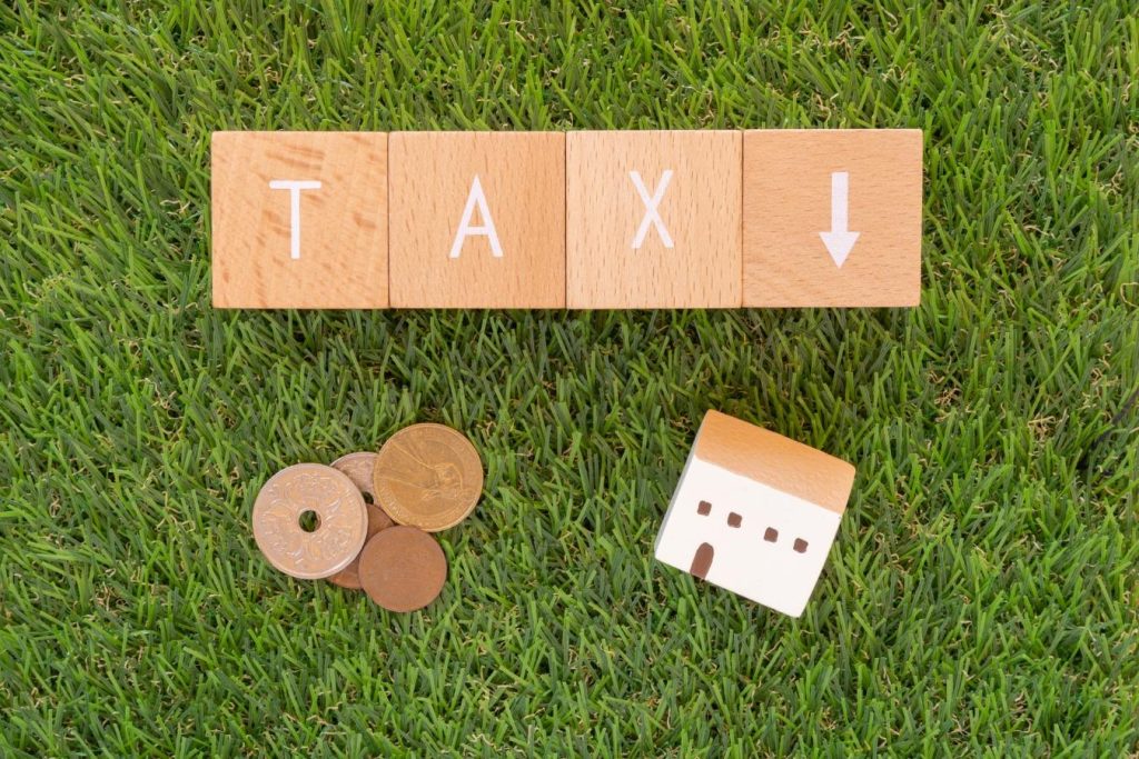 TAXの文字と下向き矢印が書かれた積み木と小銭、家のミニチュア