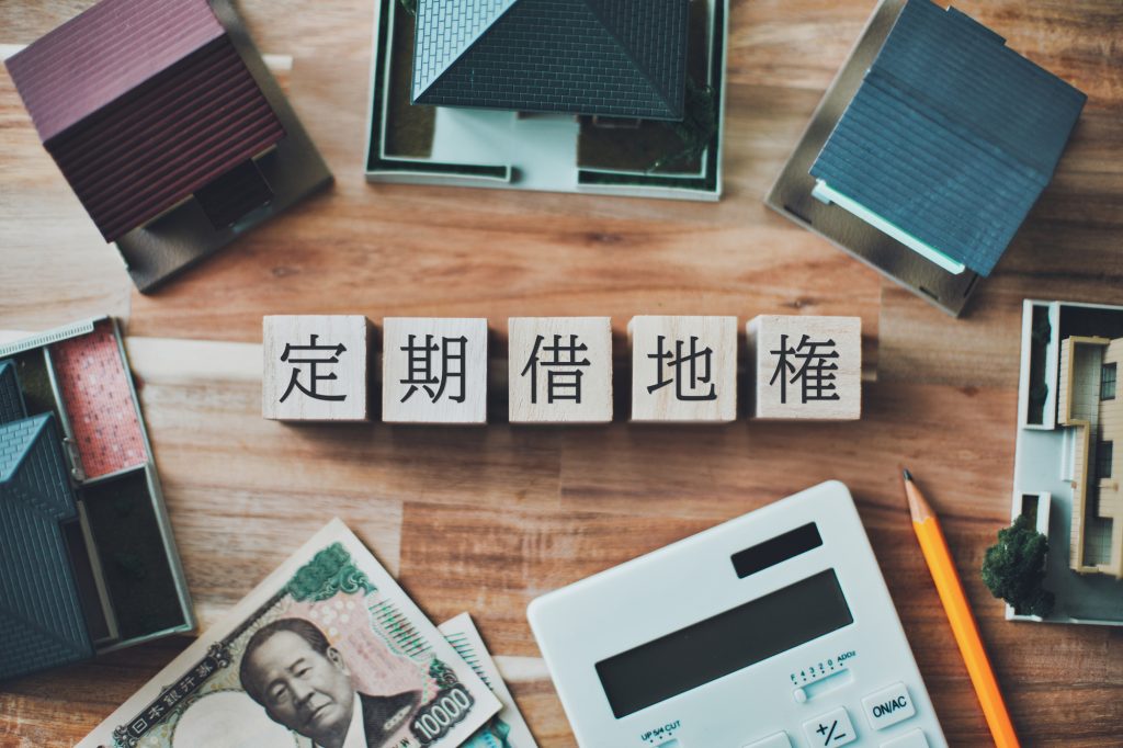 定期借地権と書かれた木製ブロックの周りに、家の模型、1万円札、電卓、鉛筆が並んでいる様子