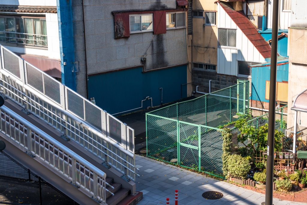 路地裏のフェンスで囲まれた小さな空き地と古い建物の外観