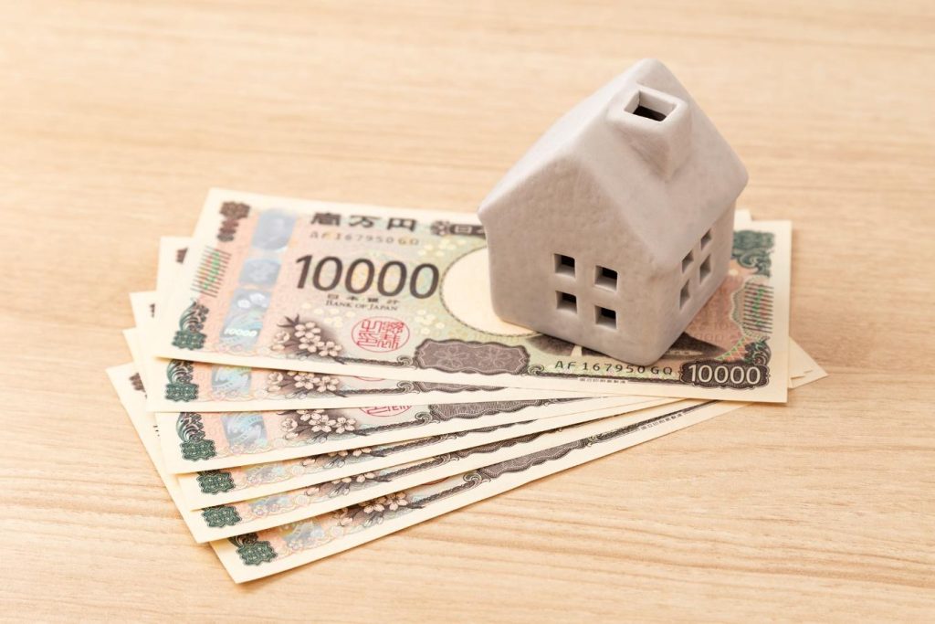 テーブルの上にある陶器でできた小さな家と下に置かれた数枚の1万円札