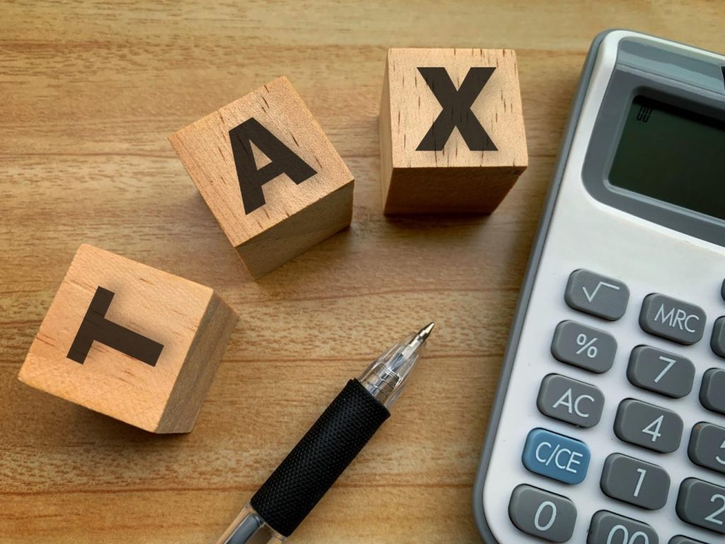 木の机に置かれた「TAX」と書かれた積み木、ペン、電卓