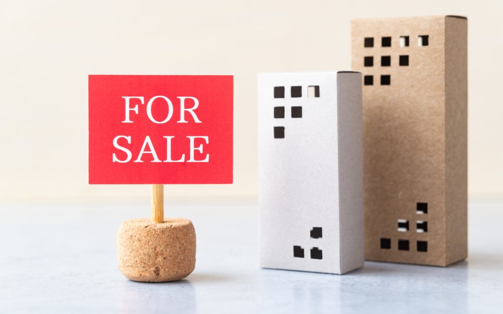 「FOR SALE」の赤い看板と建物の模型