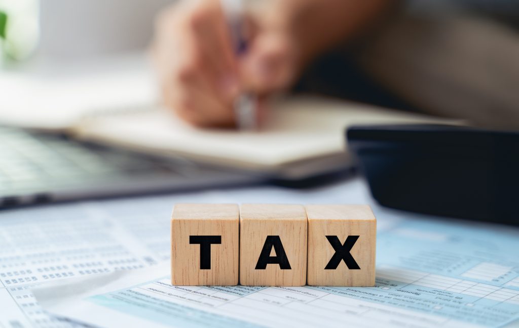 税務書類の上に置かれた「TAX」の積み木と記帳する手元