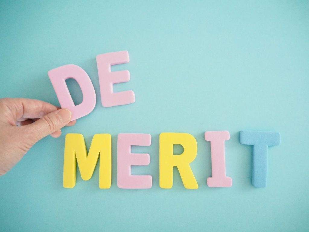 「DEMERIT」と並ぶ文字と「D」を持つ手