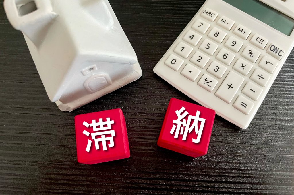 「滞納」と書かれた赤いブロックと家の模型、電卓