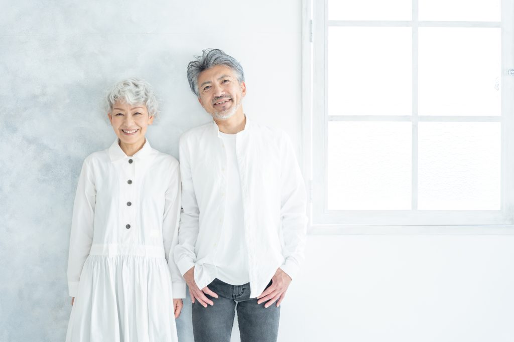 窓際に並んで立ち、笑顔を浮かべるシニア夫婦
