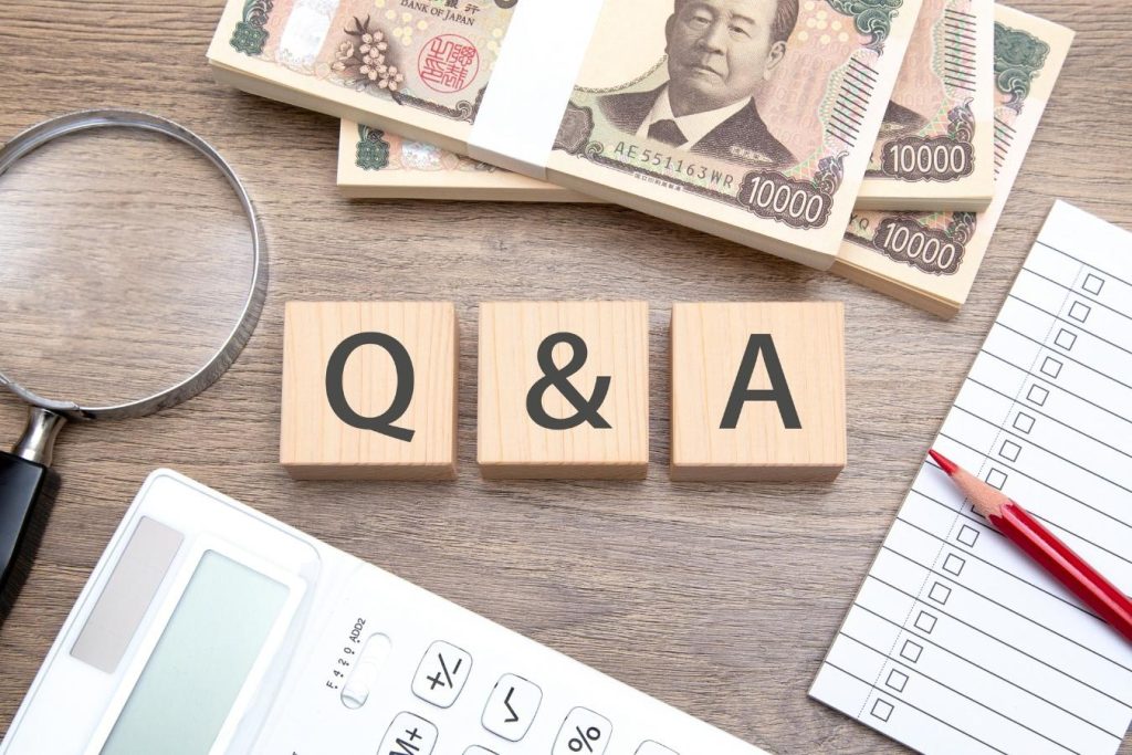 「Q&A」と書かれたブロックと周囲の札束、電卓、チェックリスト、赤鉛筆、虫メガネ