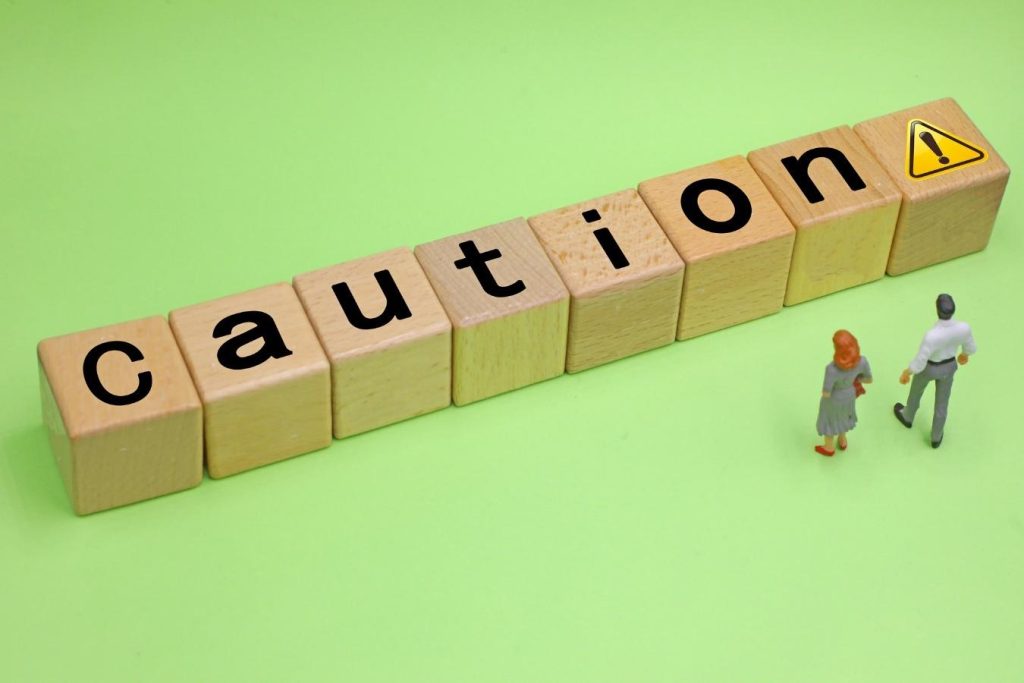 「Caution」の文字と注意マークが描かれたブロックの前に立つ男女の小さな人形