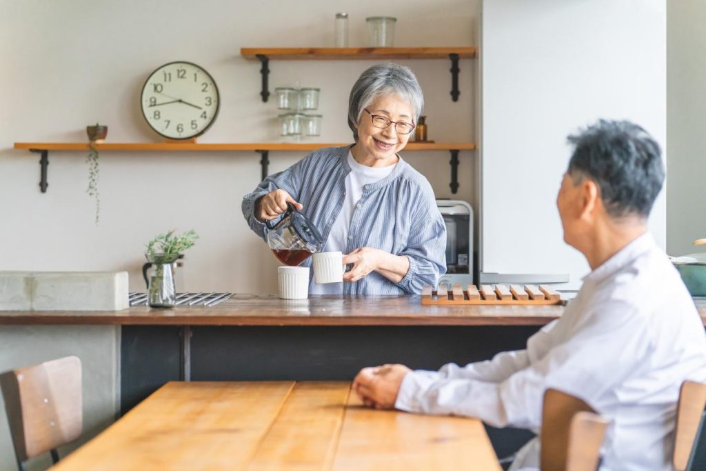 コーヒーを淹れるシニア女性とテーブルで待つシニア男性