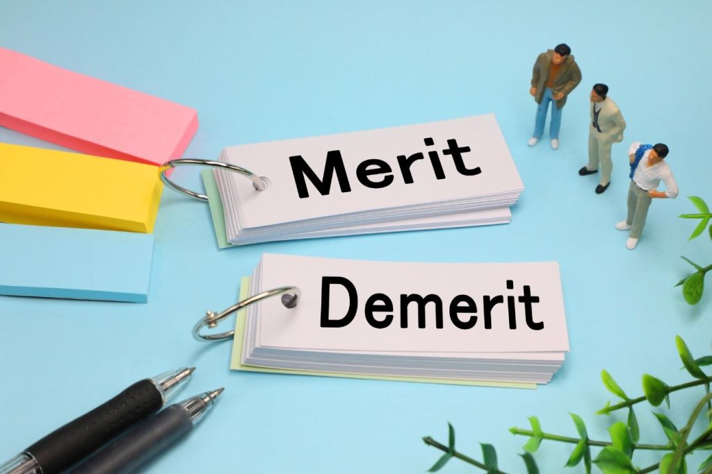 「Merit」「Demerit」と書かれた単語帳とミニチュアの人形