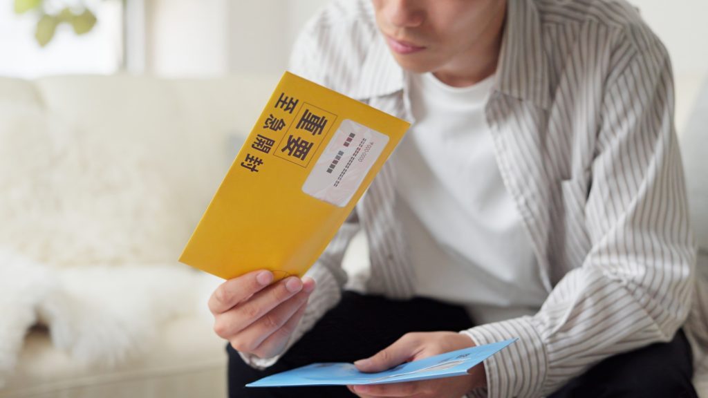 固定資産税の督促状が入った黄色い封筒を確認する男性