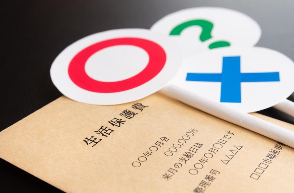 「生活保護費」と書かれた封筒と「〇」「×」「？」の札