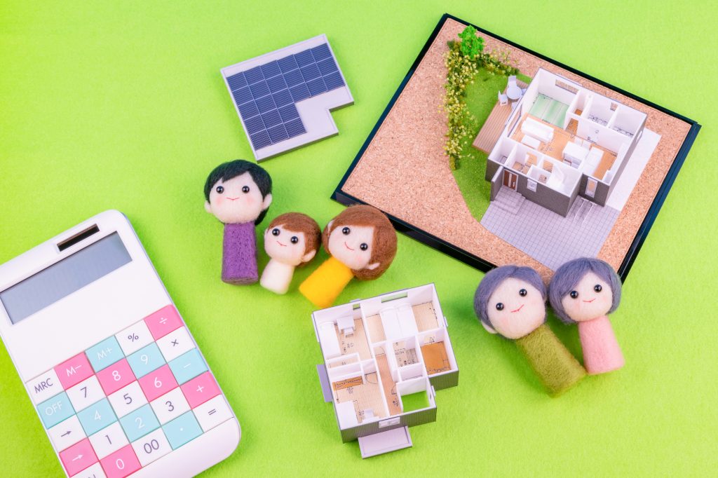 家の模型や間取り模型、電卓と家族を表す人形が並ぶイメージ