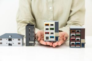 いくつか並んだ住宅模型と、そのうちひとつの模型を持つ手元