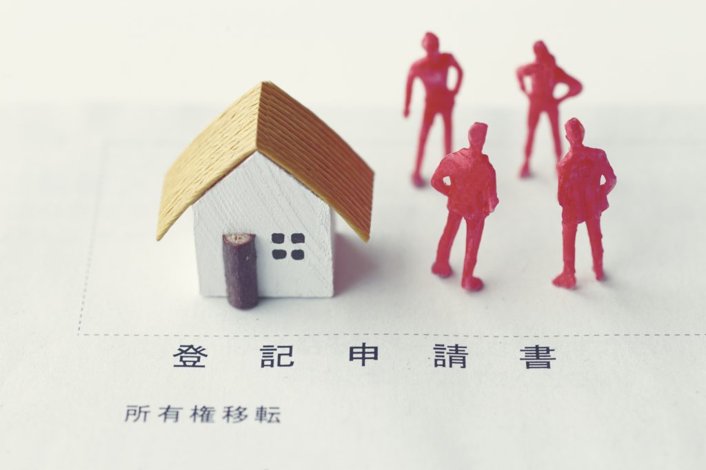家の模型と人形が並び、登記申請書の上に置かれているイメージ