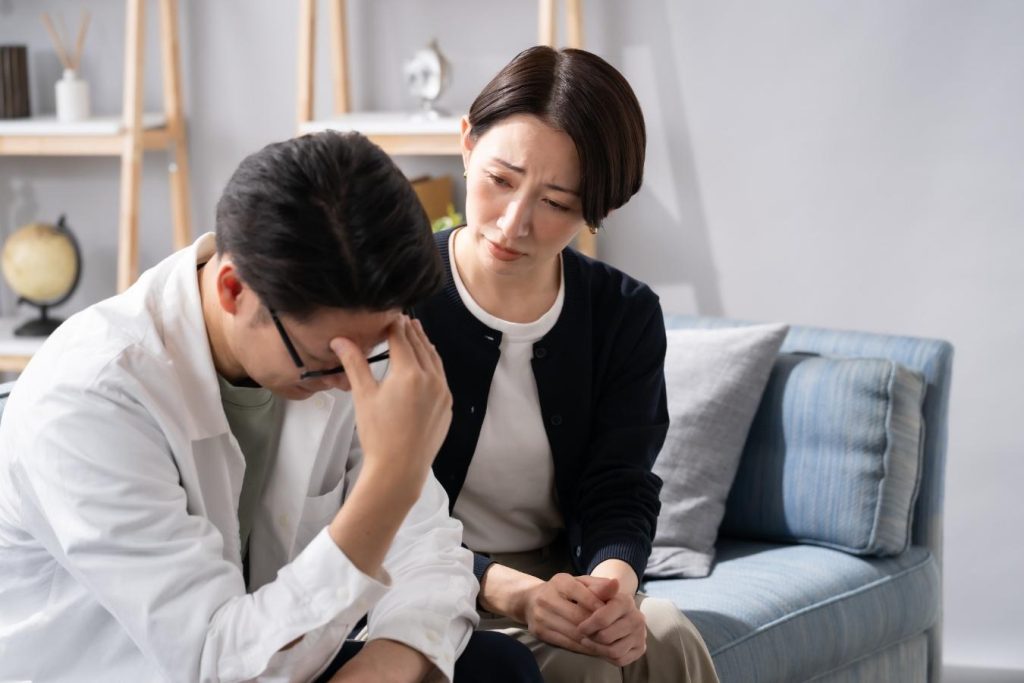 ソファに座り、額に手を当てて困っている夫婦