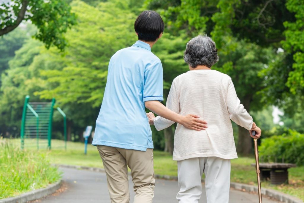 杖を使うシニア女性と介護士の後ろ姿