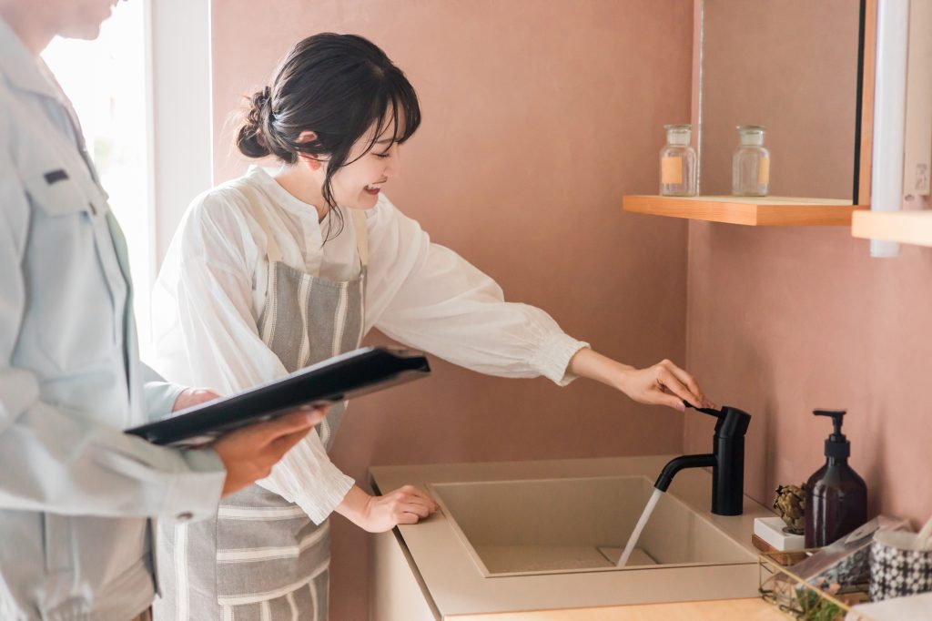 女性がキッチンの水栓を操作し、隣で作業着姿の人物がタブレットを持っているシーン