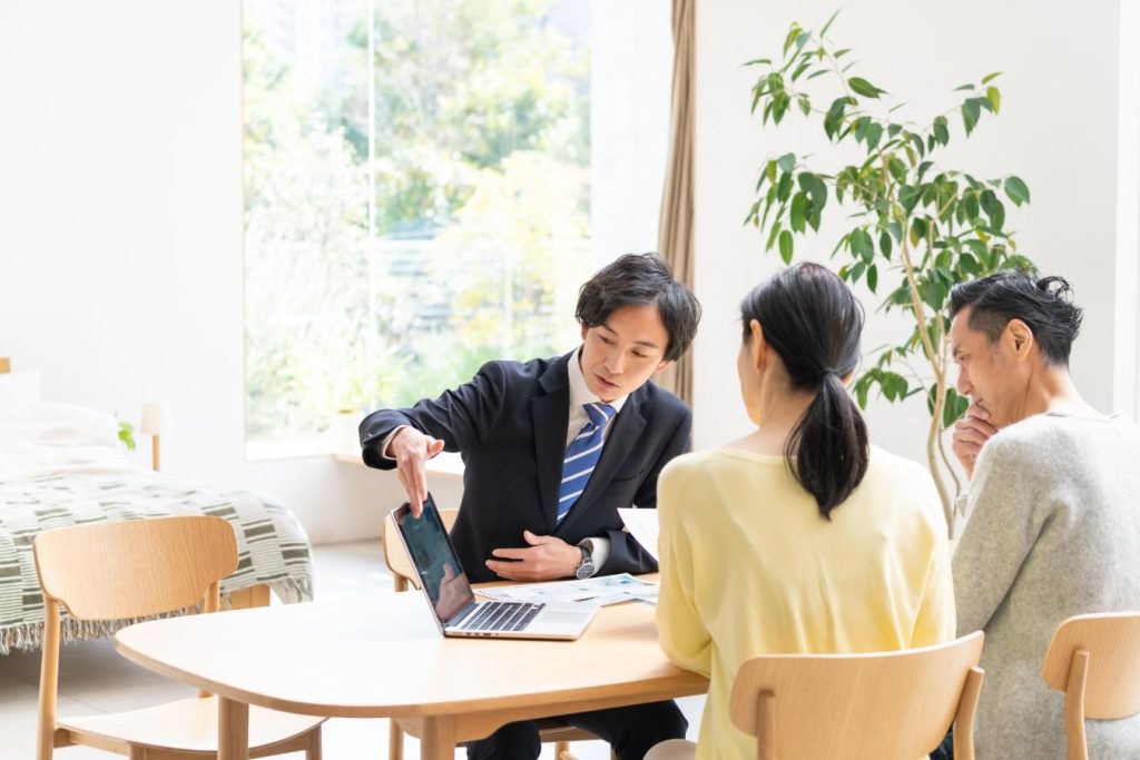 パソコン画面を見せながら説明する営業担当者と向かいに座る夫婦