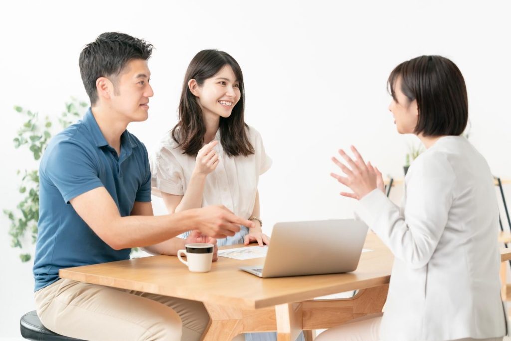 ノートパソコンを見ながら話し合うスーツ姿の女性と若い夫婦