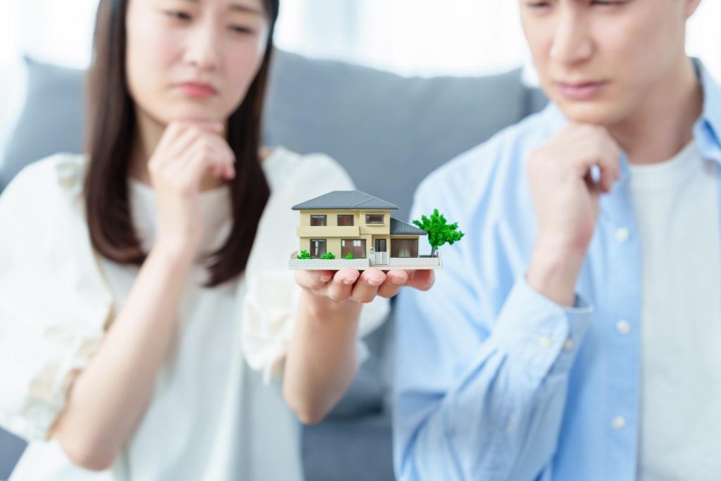 家の模型を手に乗せて考え込む夫婦