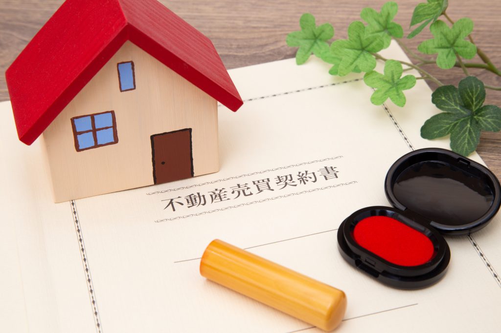 不動産売買契約書と住宅模型、印鑑を配置した写真