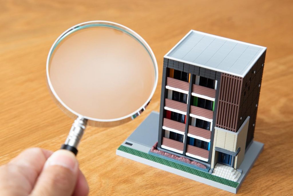 マンションの模型と虫眼鏡を持つ手元
