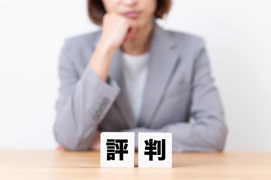 「評判」と書かれたブロックを前に、口コミや評価について考える女性のイメージ