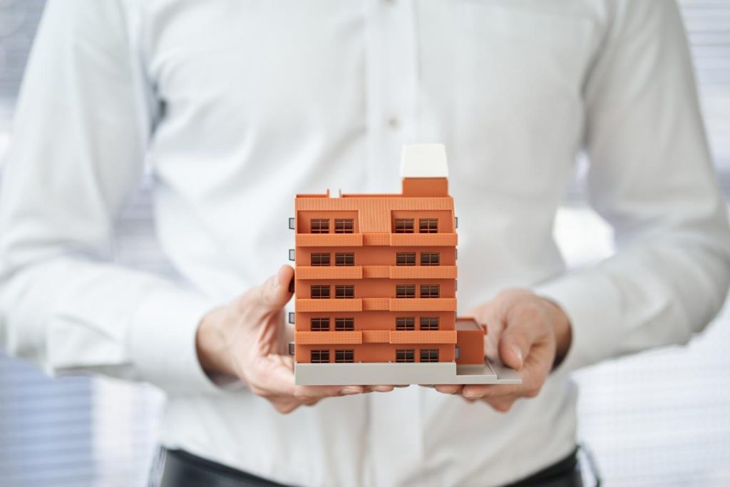 マンションの模型を両手で持つ男性の手元
