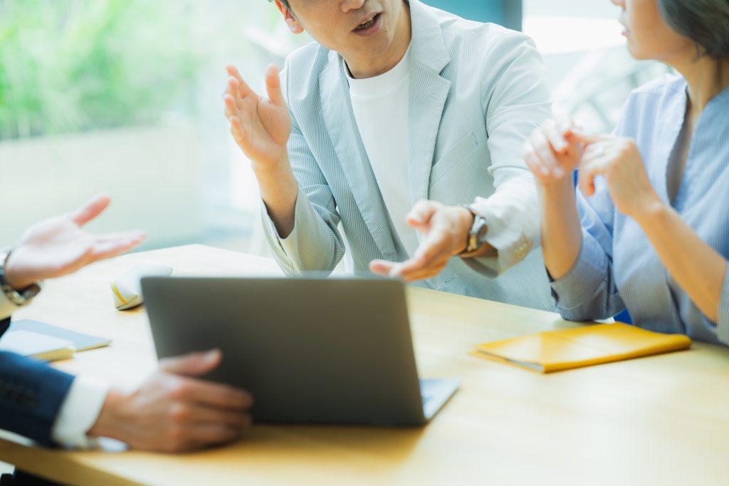 ノートパソコンを囲んで3人が身振りを交えながら話している様子