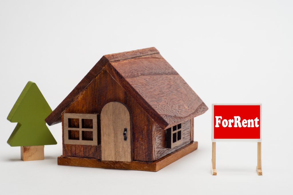 賃貸物件をイメージした木製の家と、「ForRent」の看板が並ぶイメージ