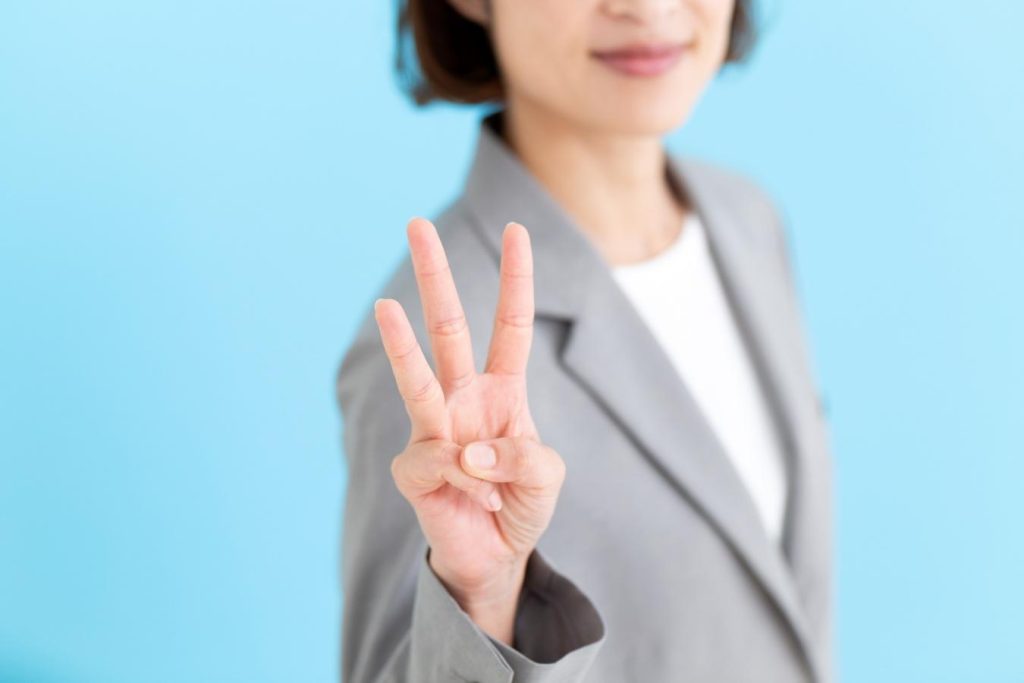 グレーのスーツを着て3本指を立てた女性