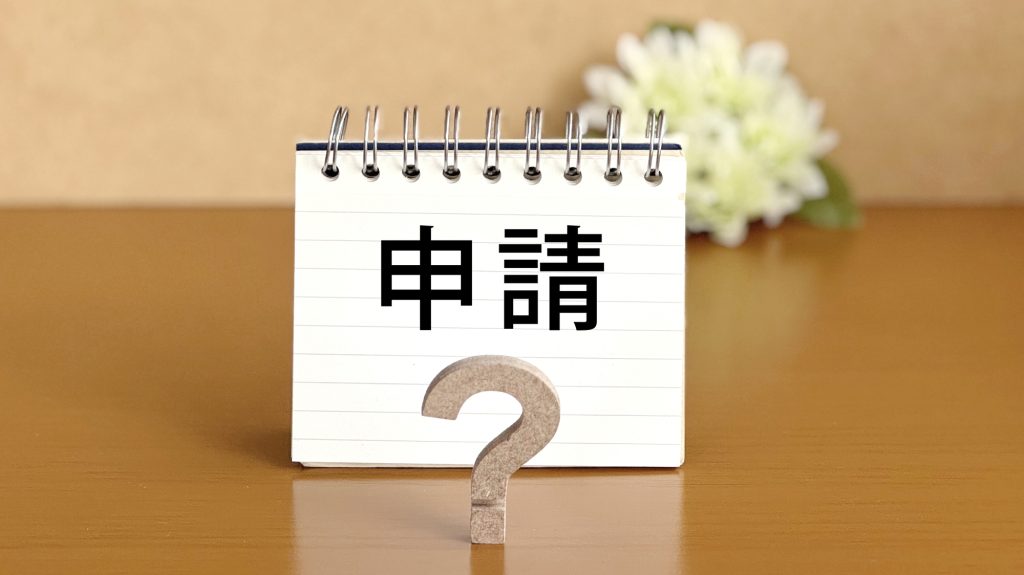 「申請」と書かれた卓上ノートと、手前に置かれたクエスチョンマークのオブジェ