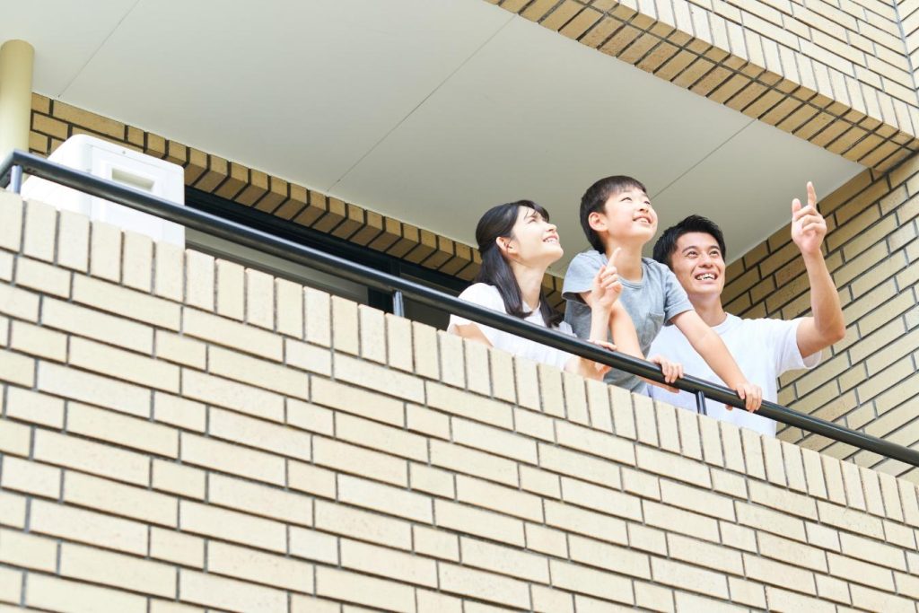 マンションのベランダから外を眺める3人家族