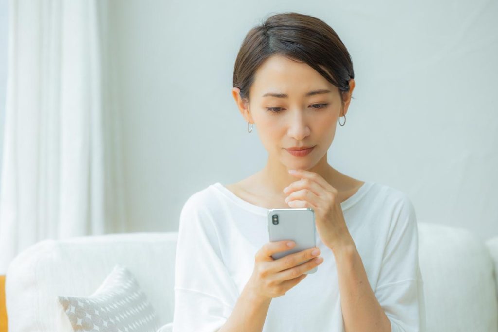 自宅のリビングで、真剣な顔でスマホを操作する女性