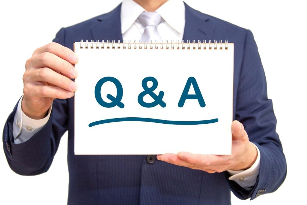 「Q&A」と書かれたスケッチブックを持つスーツの男性の手元