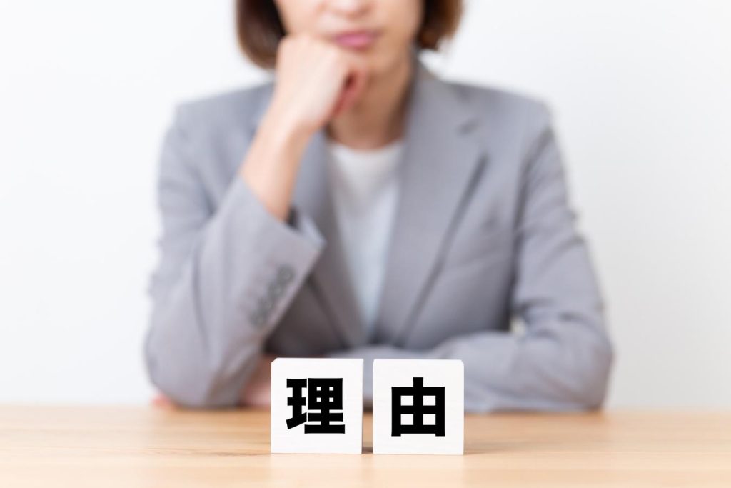 理由と書かれたブロックと悩む女性。