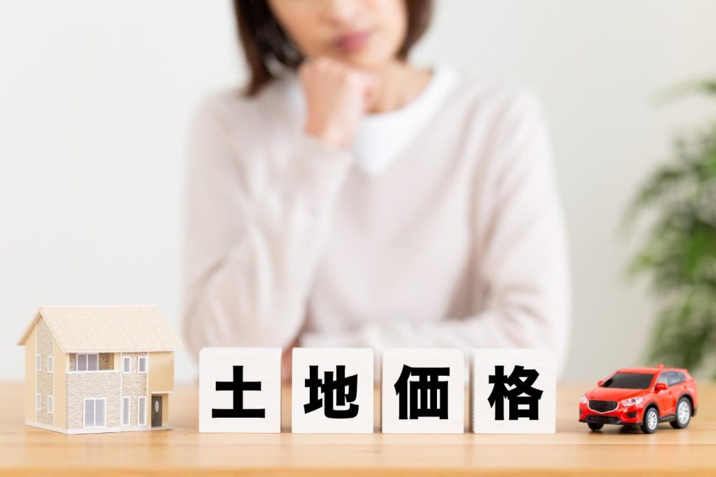 土地価格と書かれたブロックと悩む女性。
