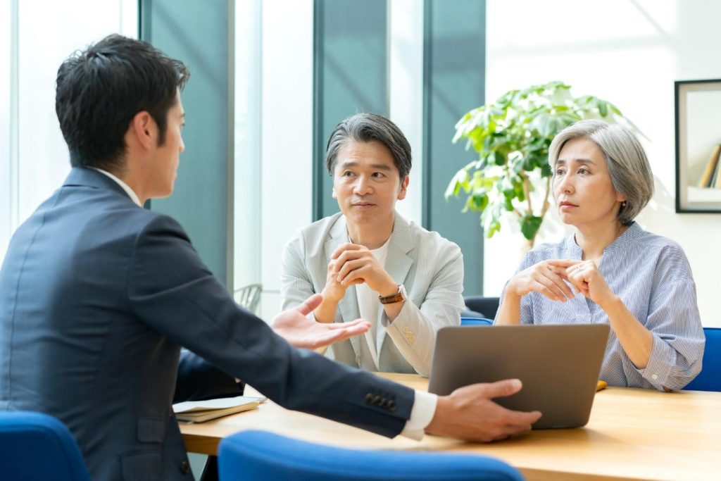 パソコンを見ながらシニア夫婦に説明をするスーツの男性