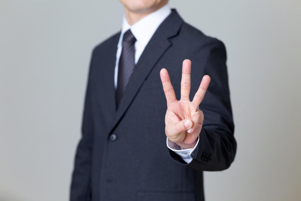3本指を前方へ突き出すビジネスパーソン。