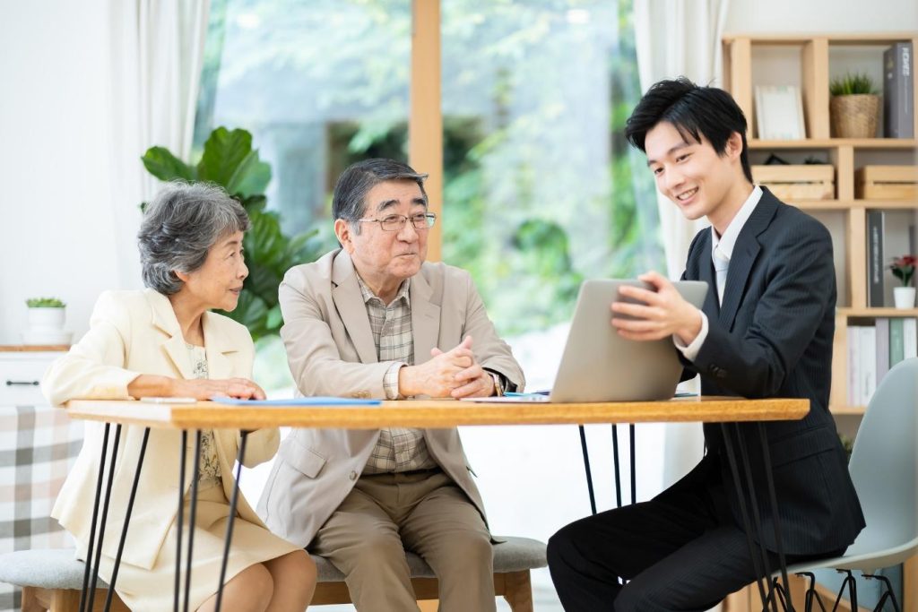 自宅のダイニングでスーツの男性に相談するシニア夫婦