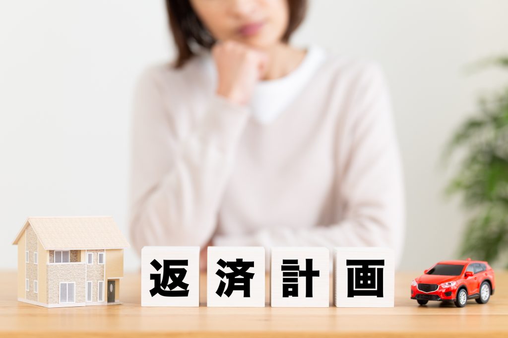 住宅ローンの返済計画について考える人と住宅模型・自動車のイメージ