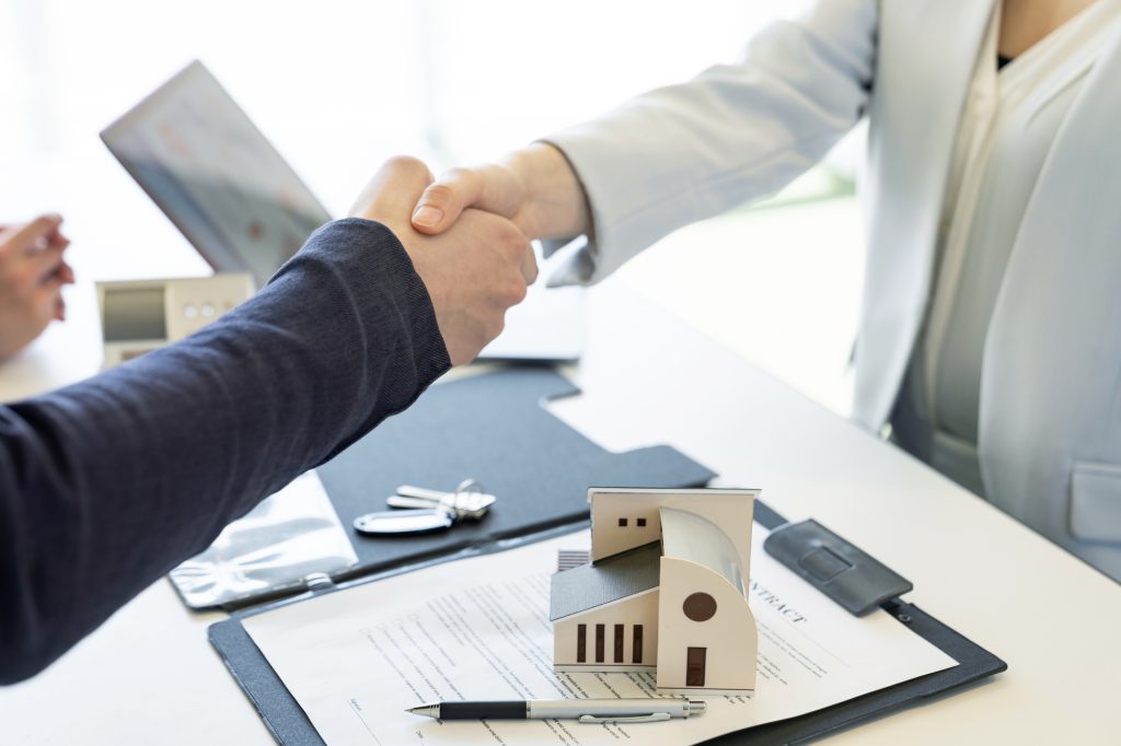 住宅模型を挟んで握手する不動産契約の場面