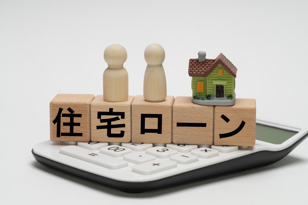電卓の上に置かれた「住宅ローン」の文字ブロックと家の模型