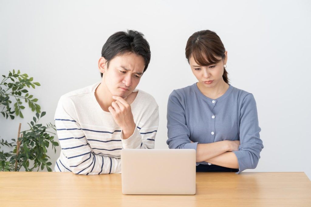 パソコンを見ながら考え事をする夫婦。
