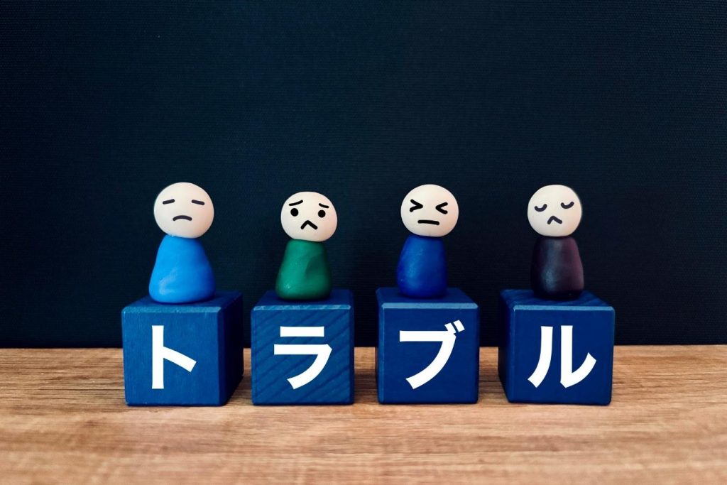 「トラブル」と書かれたブロックとその上に置かれた困った顔をした人の模型