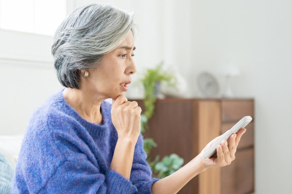 スマートフォンを見て、困った顔をするシニア女性