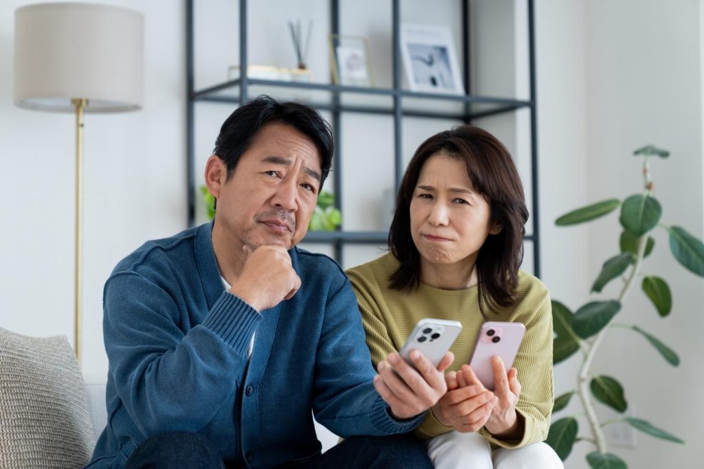 スマートフォンを見ながら悩む夫婦。